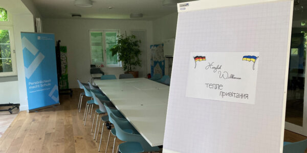 Blick in einen Seminarraum mit einem Willkommenssschild auf Deutsch und Ukrainisch.